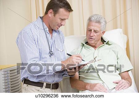 Stock Photograph - Doctor writing on clipboard while giving man checkup in exam room. Fotosearch