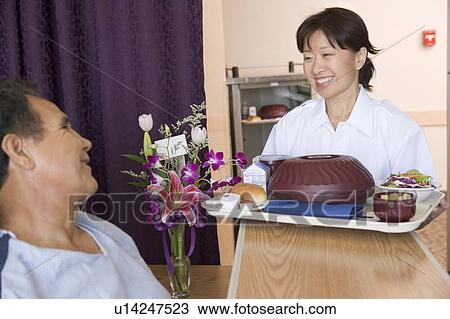 Stock Image - Nurse Serving A Patient A Meal In His Bed. Fotosearch