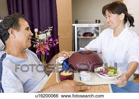 Stock Photograph - Nurse Serving A Patient A Meal In His Bed. Fotosearch