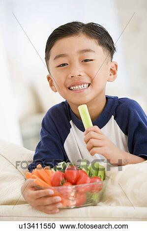 Young boy eating bowl of vegetables in living room smiling View Large Photo Image Stock Image - Young boy eating bowl of vegetables in living room smiling. Fotosearch