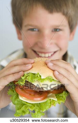 Young boy eating cheeseburger smiling View Large Photo Image Picture - Young boy eating cheeseburger smiling. Fotosearch