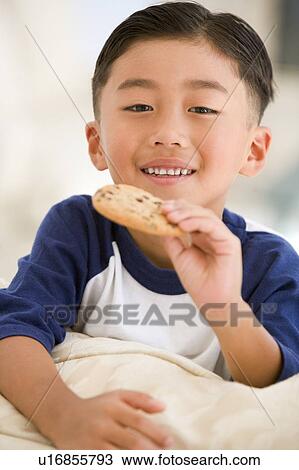 Stock Image - Young boy eating cookie in living room smiling. Fotosearch