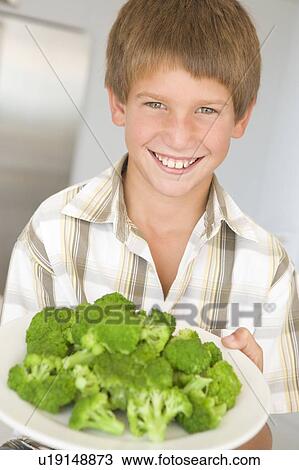 Young boy in kitchen eating broccoli smiling View Large Photo Image Stock Image - Young boy in kitchen eating broccoli smiling. Fotosearch