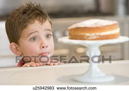Stock Image - Young boy in kitchen looking at cake on counter. Fotosearch