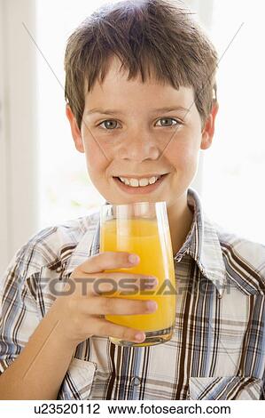 Stock Image - Young boy indoors drinking orange juice smiling. Fotosearch