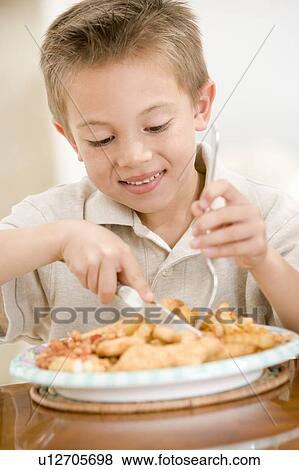 Stock Photo - Young boy indoors eating fish and chips smiling. Fotosearch