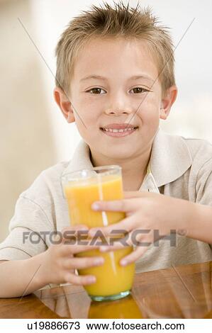 Stock Image - Young boy indoors with orange juice smiling. Fotosearch