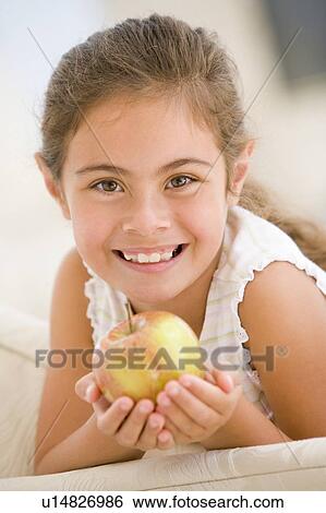 Young girl eating apple in living room smiling View Large Photo Image Stock Photograph - Young girl eating apple in living room smiling. Fotosearch