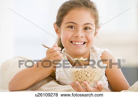 Young girl eating cereal in living room smiling View Large Photo Image Stock Photo - Young girl eating cereal in living room smiling. Fotosearch