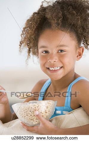 Young girl eating cereal in living room smiling View Large Photo Image Stock Photo - Young girl eating cereal in living room smiling. Fotosearch
