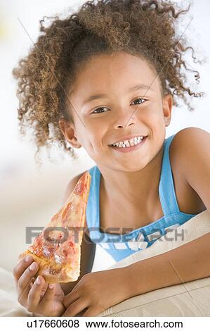 Young girl eating pizza slice in living room smiling View Large Photo Image Stock Photo - Young girl eating pizza slice in living room smiling. Fotosearch