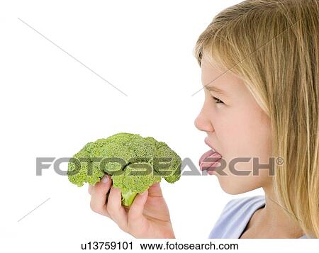 Stock Image - Young girl holding broccoli and sticking tongue out. Fotosearch