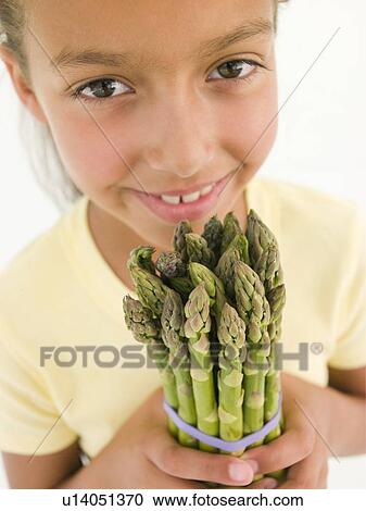 Stock Image - Young girl holding bunch of asparagus and smiling. Fotosearch