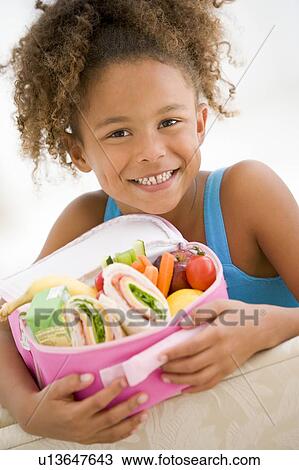 Young girl holding packed lunch in living room smiling View Large Photo Image Stock Image - Young girl holding packed lunch in living room smiling. Fotosearch