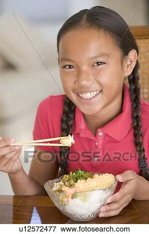 Young girl in dining room eating Chinese food smiling View Large Photo Image Stock Photo - Young girl in dining room eating Chinese food smiling. Fotosearch