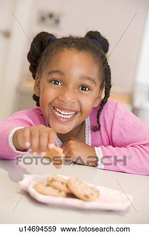 Young girl in kitchen eating cookies smiling View Large Photo Image Stock Photo - Young girl in kitchen eating cookies smiling. Fotosearch