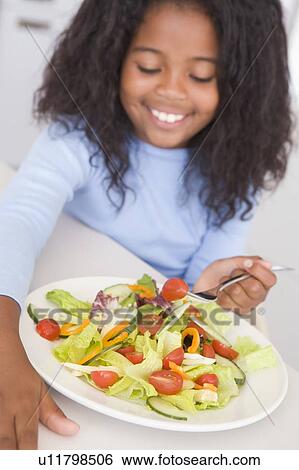 Stock Photograph - Young girl in kitchen eating salad smiling. Fotosearch