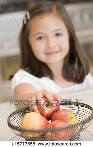 Young girl in kitchen getting apple off counter smiling View Large Photo Image Stock Photo - Young girl in kitchen getting apple off counter smiling. Fotosearch
