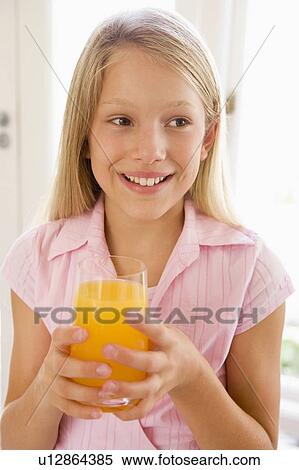 Stock Photography - Young girl indoors drinking orange juice smiling. Fotosearch