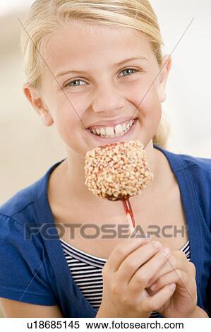 Young girl indoors eating candy apple smiling View Large Photo Image Stock Photography - Young girl indoors eating candy apple smiling. Fotosearch