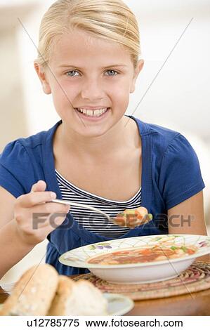 Stock Photography - Young girl indoors eating soup smiling. Fotosearch