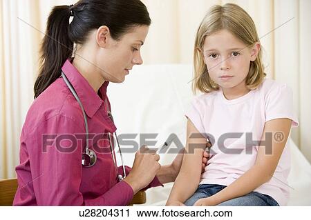 Stock Image - Doctor giving needle to young girl in exam room. Fotosearch