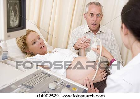 Stock Photo - Pregnant woman getting ultrasound from doctor with husband watching. Fotosearch