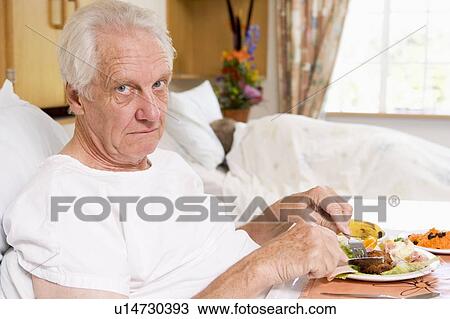 Stock Image - Senior Man Eating Hospital Food In Bed. Fotosearch
