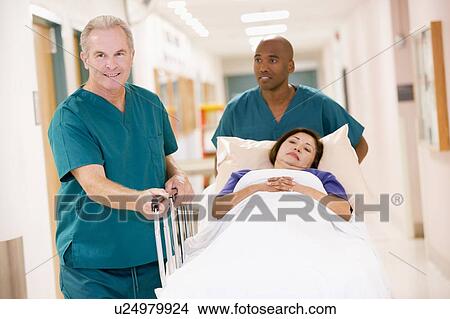 Picture - Two Orderlies Pushing A Woman In A Bed Down A Hospital Corridor. Fotosearch