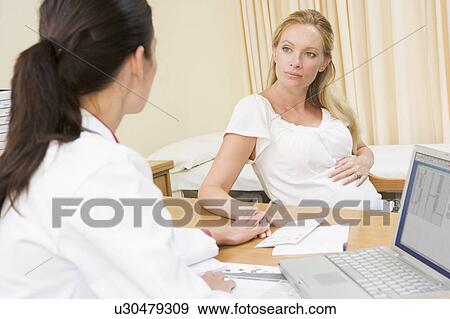 Stock Photo - Doctor with laptop and pregnant woman in doctor's office. Fotosearch