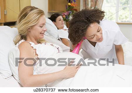 Stock Photo - Nurse checking pregnant woman's belly and smiling. Fotosearch