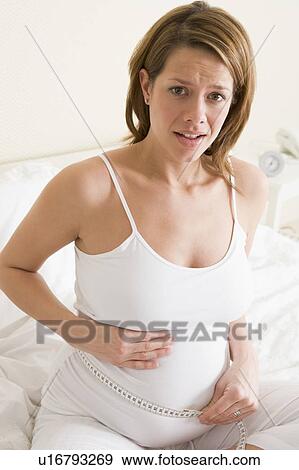 Pregnant woman in bedroom measuring belly looking worried View Large Photo Image Stock Photo - Pregnant woman in bedroom measuring belly looking worried. Fotosearch