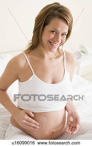 Pregnant woman in bedroom rubbing cream on belly smiling View Large Photo Image Stock Photograph - Pregnant woman in bedroom rubbing cream on belly smiling. Fotosearch