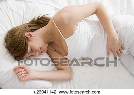 Stock Image - Pregnant woman lying in bed sleeping. Fotosearch