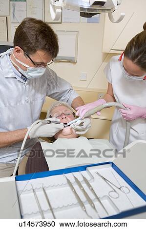 Stock Image - Dentist and assistant in exam room with woman in chair. Fotosearch
