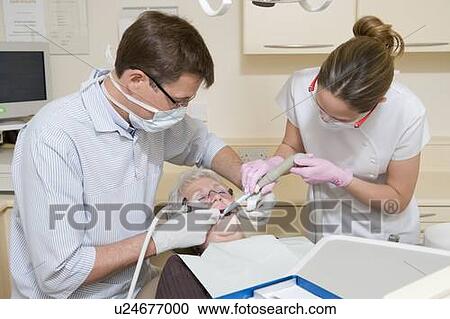 Dentist and assistant in exam room with woman in chair View Large Photo Image Stock Image - Dentist and assistant in exam room with woman in chair. Fotosearch