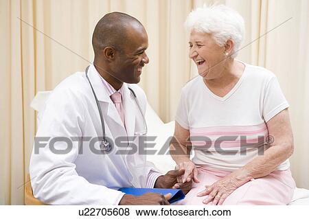 Doctor giving checkup to woman in exam room smiling View Large Photo Image Stock Photo - Doctor giving checkup to woman in exam room smiling. Fotosearch