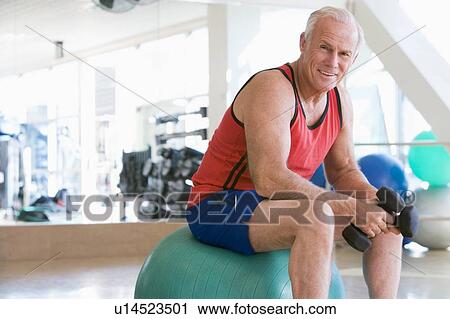 Stock Image - Man Using Hand Weights On Swiss Ball At Gym. Fotosearch