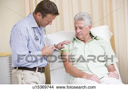 Picture - Doctor giving man needle in exam room. Fotosearch