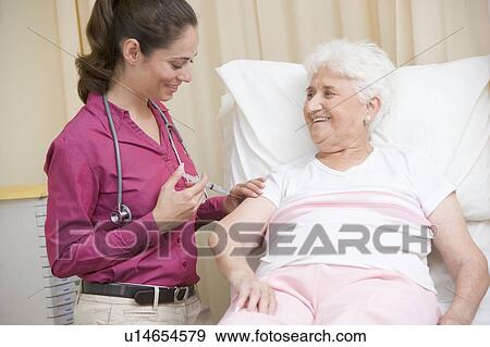 Stock Photo - Doctor giving needle to woman in exam room smiling. Fotosearch