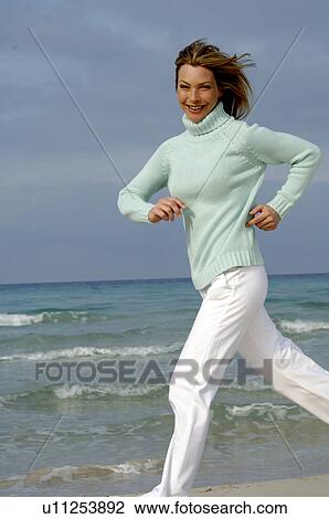 Stock Image - Running woman in turquoise pullover at the sea. Fotosearch