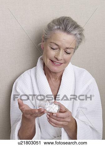 Stock Image - Senior woman holding a glass of pills. Fotosearch