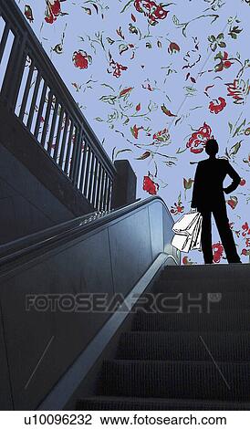 Low angle view of a woman standing on an escalator View Large Illustration Drawing - Low angle view of a woman standing on an escalator. Fotosearch