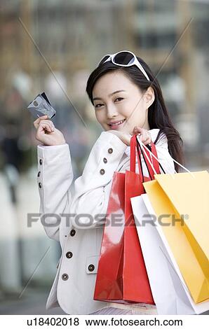 Stock Photo - Young woman holding shopping bags over shoulder with two bank cards. Fotosearch