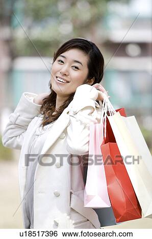 Stock Photograph - Young woman holding shopping bags over shoulder. Fotosearch