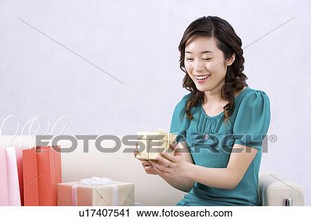 Stock Image - Young woman looking at gift, smiling. Fotosearch