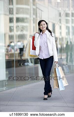 Stock Image - Young woman on the phone holding shopping bags. Fotosearch
