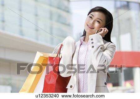 Stock Image - Young woman on the phone with shopping bags. Fotosearch
