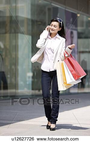 Stock Photograph - Young woman on the phone with shopping bags. Fotosearch