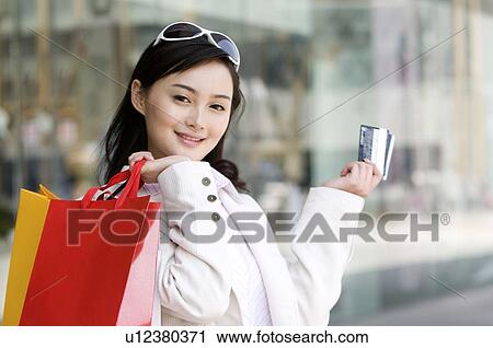Stock Image - Young woman putting shopping bags on her shoulder. Fotosearch